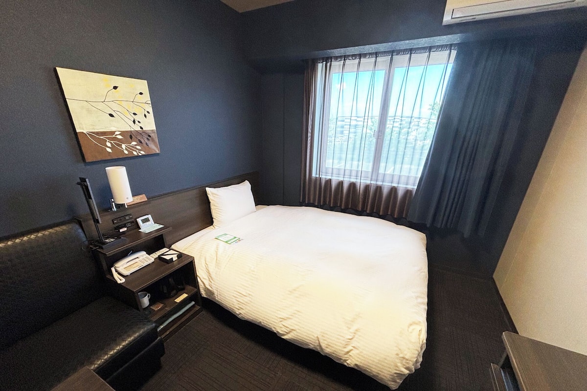 Ein Hotelzimmer mit Bett, Schreibtisch, Telefon, Lampe und einem Bild an der Wand.