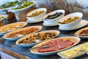 Un bufé con diversos platos, incluyendo pasta, aceitunas y carnes.