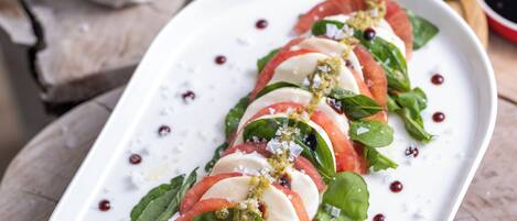A white rectangular plate with a tomato, mozzarella, and basil salad, garnished with olive oil and salt, on a wooden table.