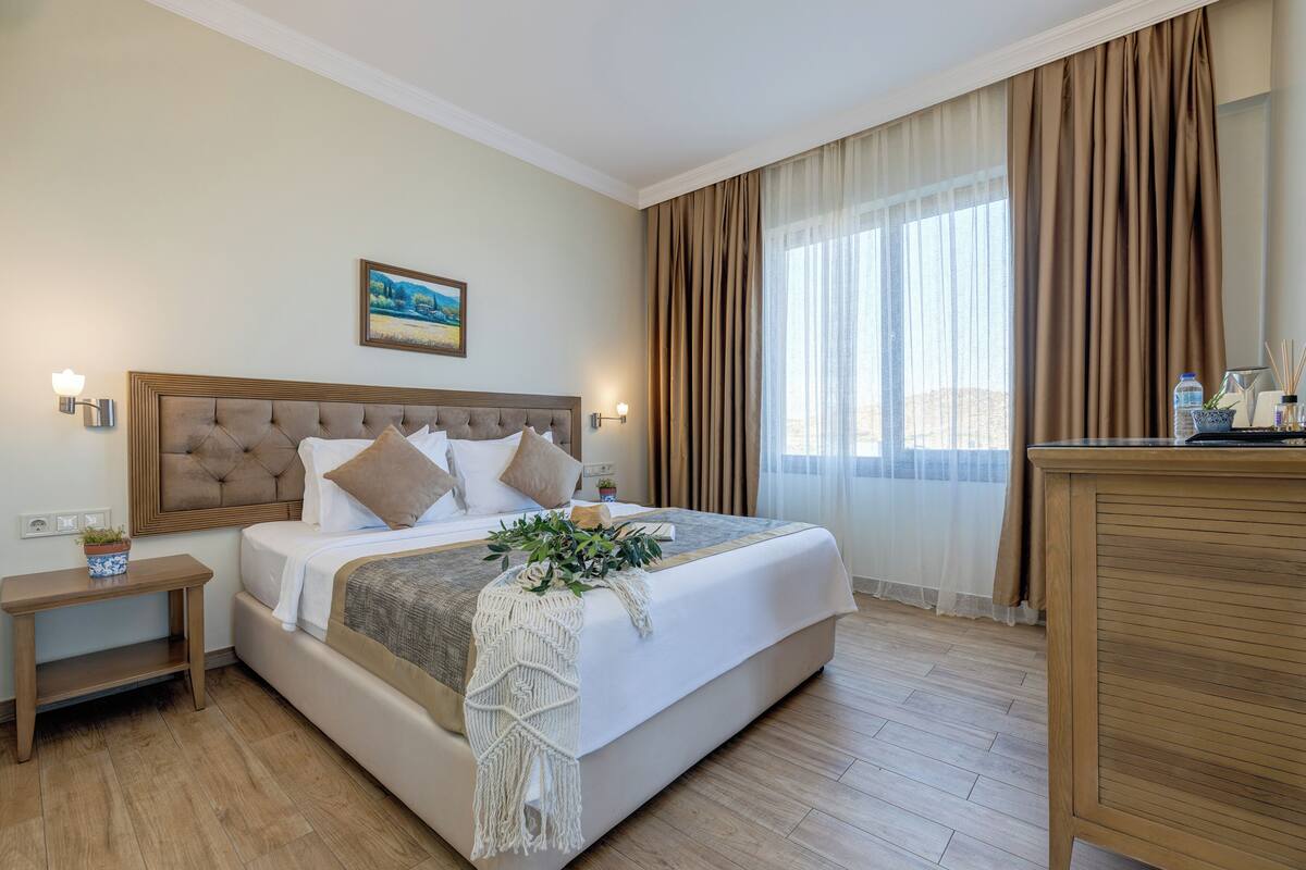A hotel room with a bed, bedside tables, a nightstand, a desk, and a window with curtains.