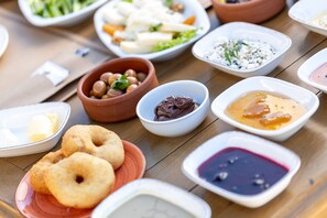 A variety of food items arranged on a wooden table, including bowls of different sauces, a plate of fried dough, and a bowl of chickpeas. - Cinarli Kasri Hotel (Gökçeada)