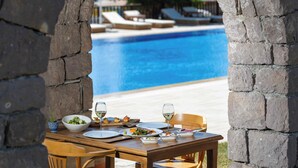 Una mesa de comedor con platos, tazones y copas de vino, con vista a una piscina.