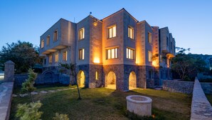 Un edificio de varios pisos con arcos de piedra y ventanas iluminadas al anochecer.