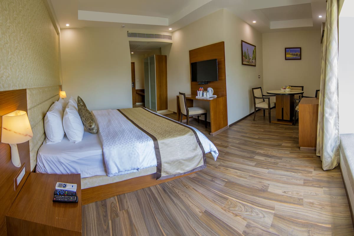 Habitació d'hotel amb llit, taula de nit, làmpada, comandament a distància, sòl de fusta, escriptori, cadira, televisió i obra d'art a la paret.