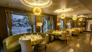 A restaurant with round tables, chairs, and chandeliers. - The India Benares (Varanasi)
