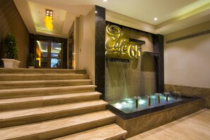 A hotel entrance with a grand staircase, a decorative wall with the hotel's name, and a water feature. - The India Benares (Varanasi)