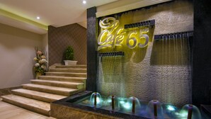 A modern lobby with a water feature, a staircase, and a neon sign reading "Café 65". - The India Benares (Varanasi)