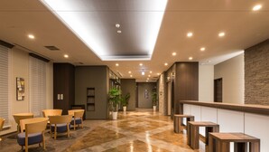 A hotel lobby with a check-in counter, seating area with chairs, a reception desk, and a staircase. - Hotel Route-Inn Grand Kitami Ekimae (Kitami)