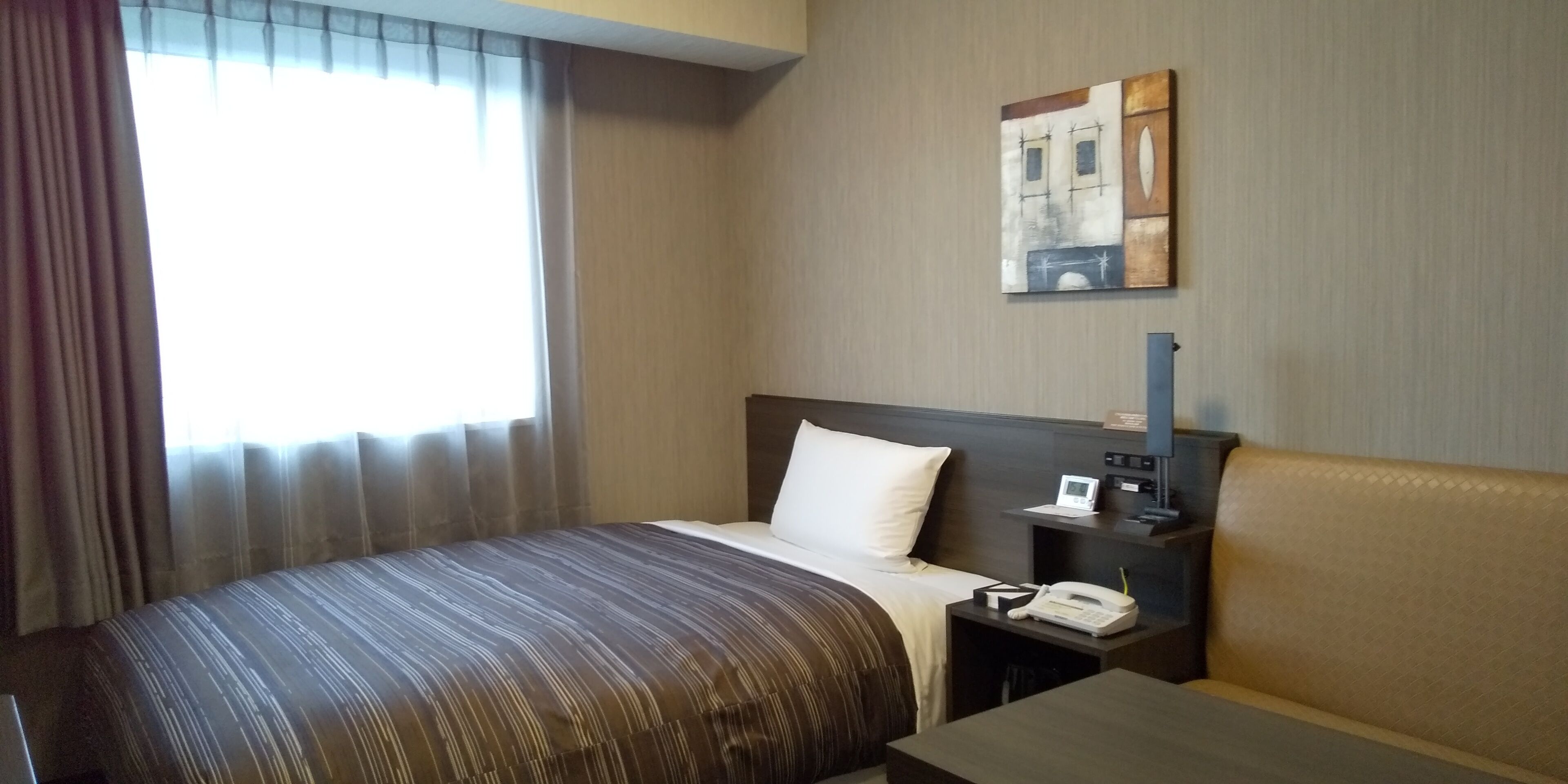 A hotel room with a bed, bedside table, and a painting on the wall.