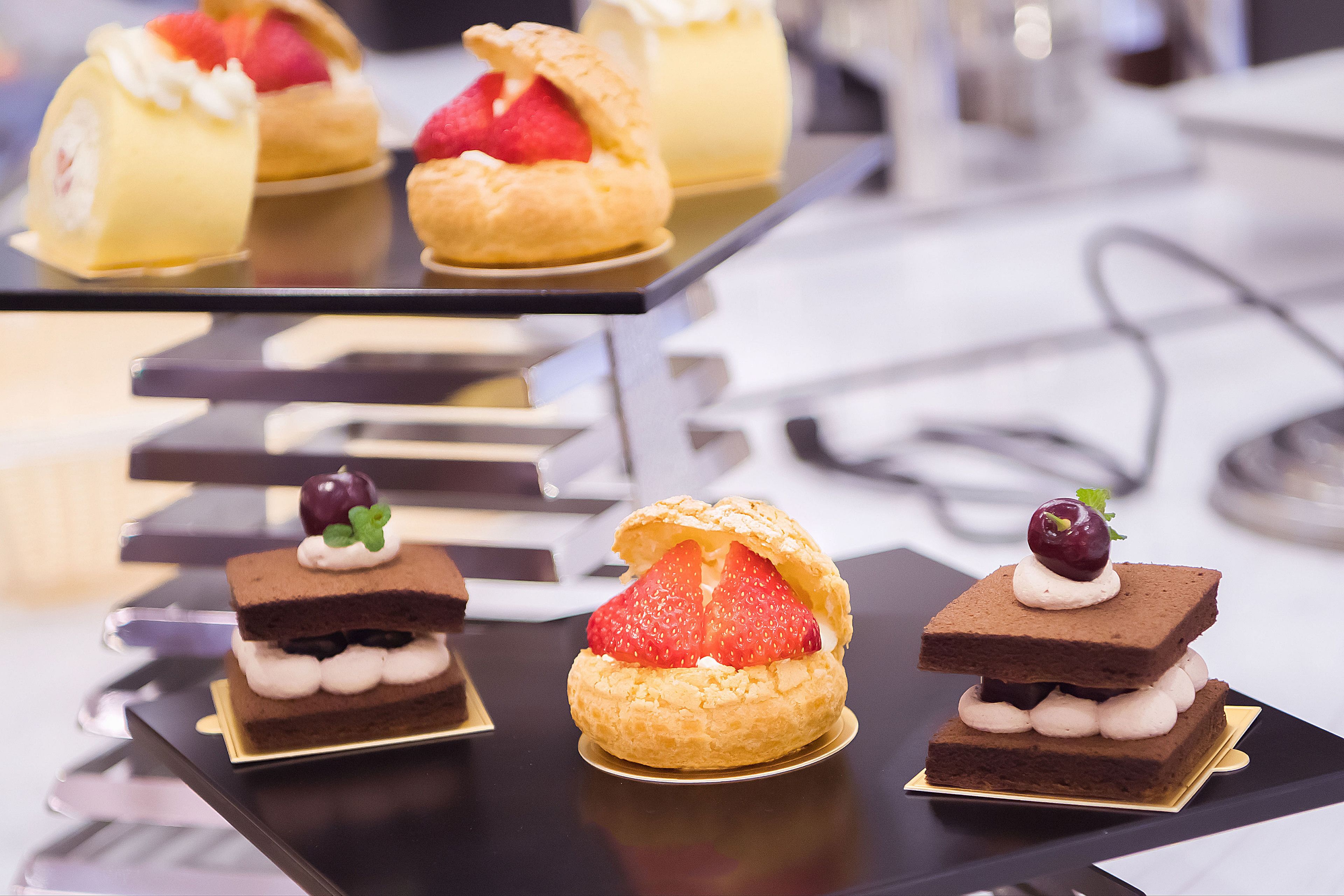 Esposizione di dolci con varie paste e torte, tra cui una pasta con fragole e una torta al cioccolato con panna montata.
