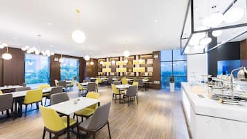 Un comedor moderno con varias mesas y sillas, una encimera de cocina y ventanas amplias que ofrecen vistas al exterior.