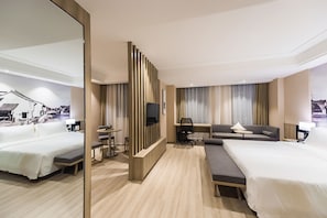 Habitación de hotel con una cama grande, un sofá, un escritorio con una silla, un televisor y un espejo.