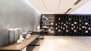 Un interior moderno con una larga mesa que exhibe objetos decorativos, una estantería con libros y una pared gris.