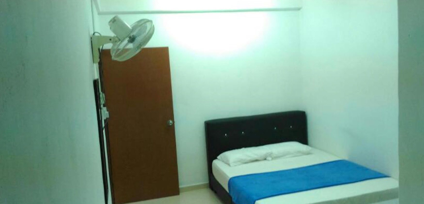 A small, simple room with a bed, a door, and a ceiling fan.