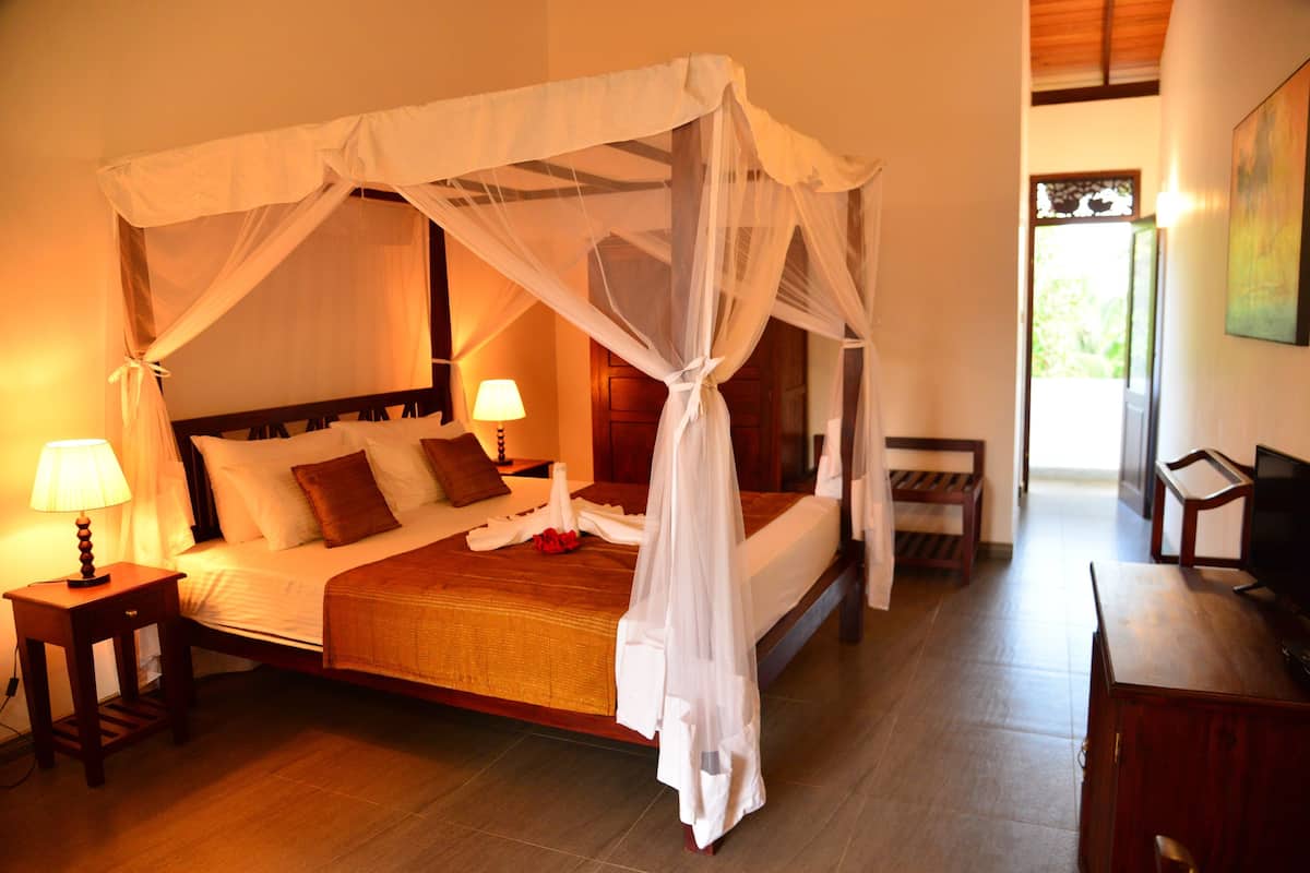 A four-poster bed with a canopy, a bedside table with a lamp, and a wooden bench.