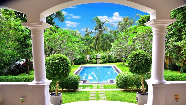 A pool with a clear view through a white archway, surrounded by lush greenery and a well-maintained lawn. - Boutique Villa Shanthi (Hikkaduwa)