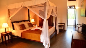 A four-poster bed with a canopy, a bedside table with a lamp, a wooden bench, and a television on a wooden stand. - Boutique Villa Shanthi (Hikkaduwa)