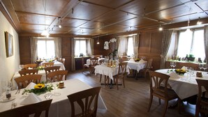 A dining area with multiple tables set for guests, wooden chairs, and a warm, wooden interior.