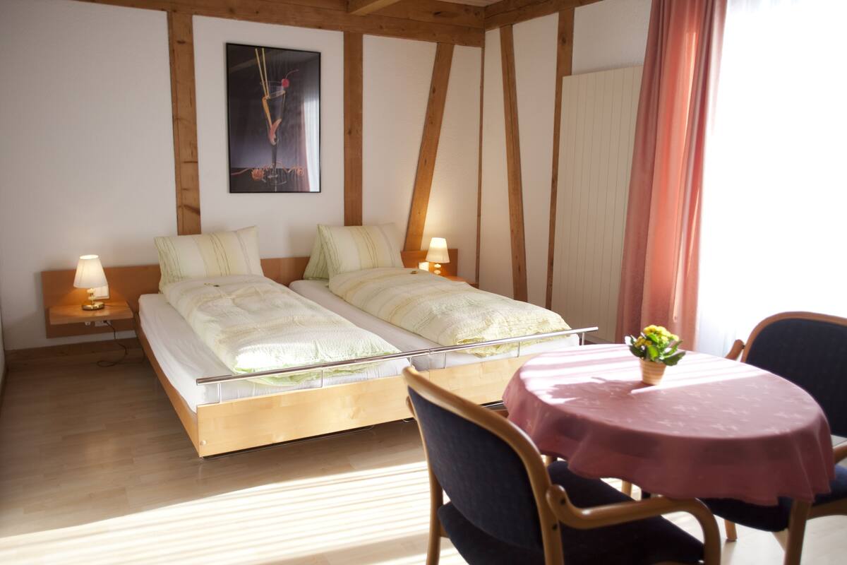 Un dormitorio con cama, lámparas de noche, una mesa con un jarrón y un cuadro en la pared.