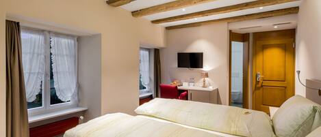 Una habitación de hotel con una cama grande, un escritorio, una silla, un televisor y techo de madera.