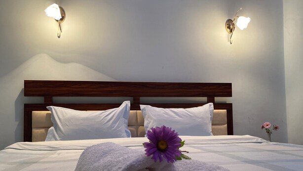 A neatly made bed with rolled white towels and a purple flower, two white pillows, and a wooden headboard. - Christy Hotel (Goris)