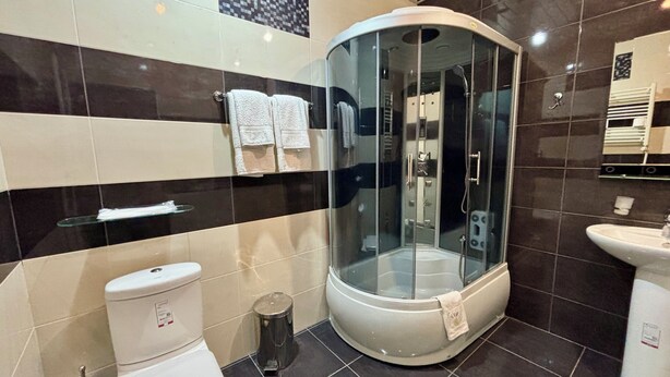 A modern bathroom with a glass-enclosed shower, a toilet, and a sink. - Christy Hotel (Goris)