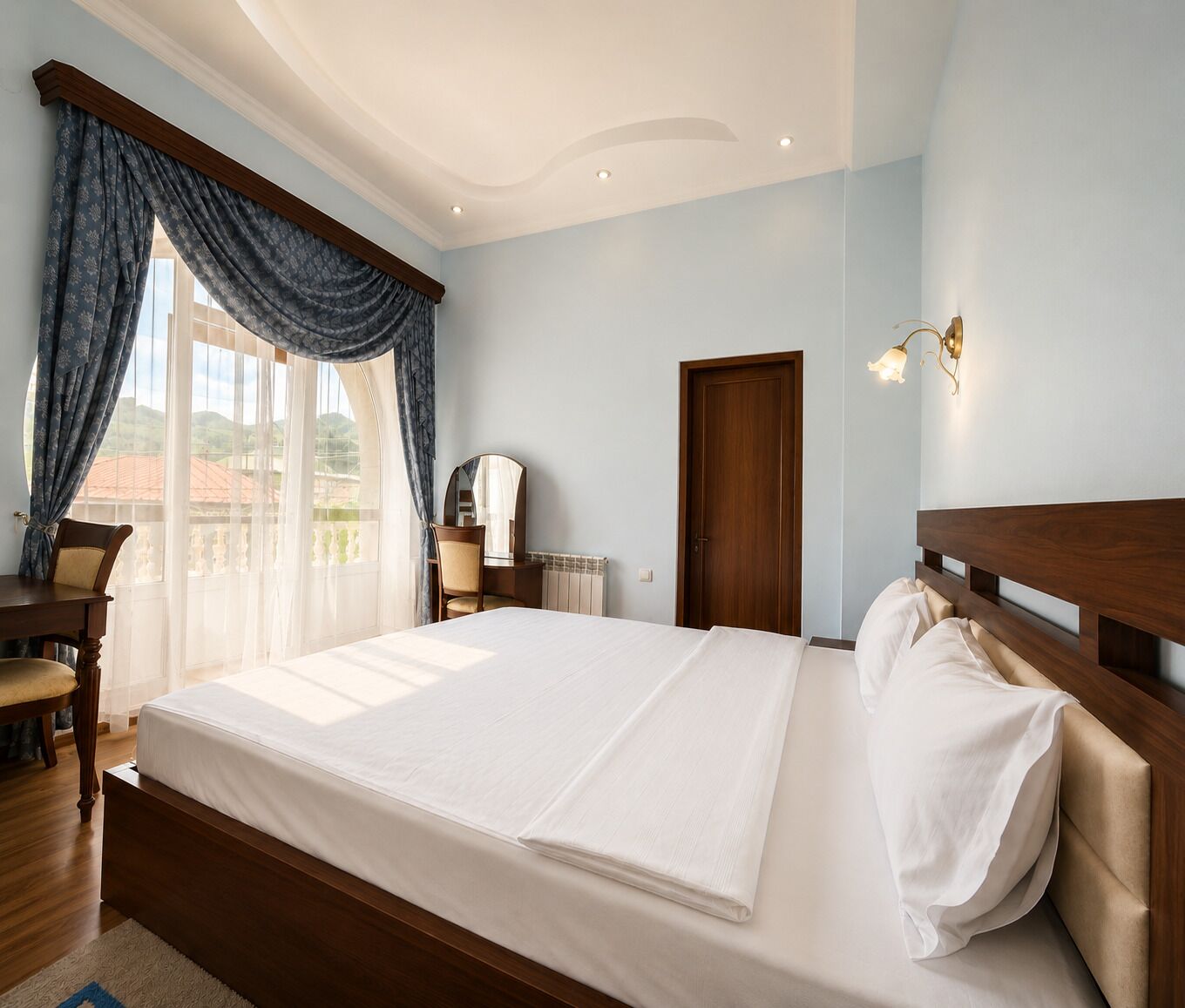 Quarto de hotel com cama grande, escrivaninha, cadeira, cômoda e vista para o exterior.