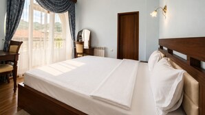 A hotel room with a large bed, a desk, a chair, a dresser, and a view of the outdoors. - Christy Hotel (Goris)