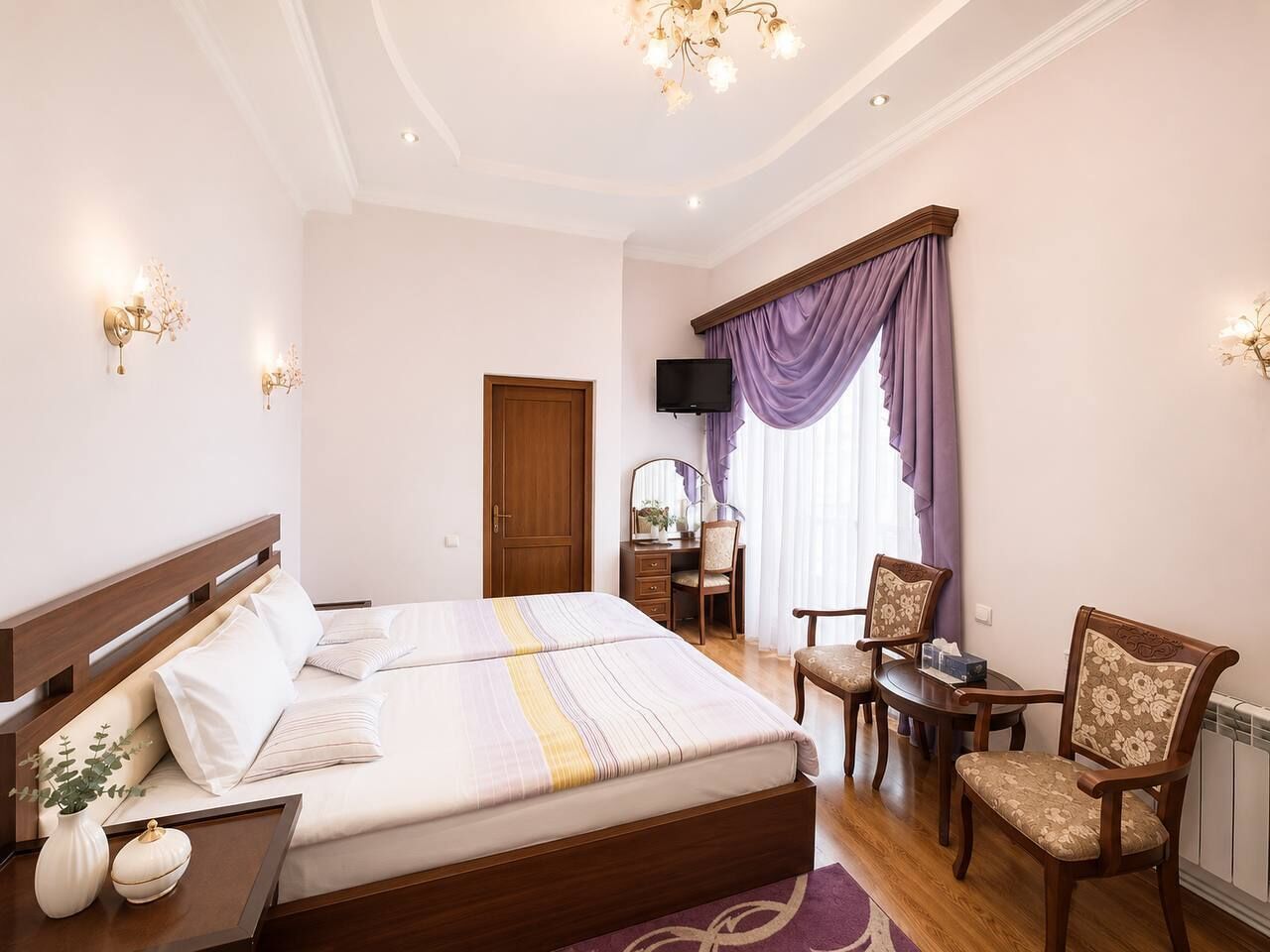 A hotel room with a double bed, a desk with a chair, a television, and a window with curtains.