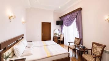 A hotel room with a double bed, a desk with a chair, a television, and a window with curtains.