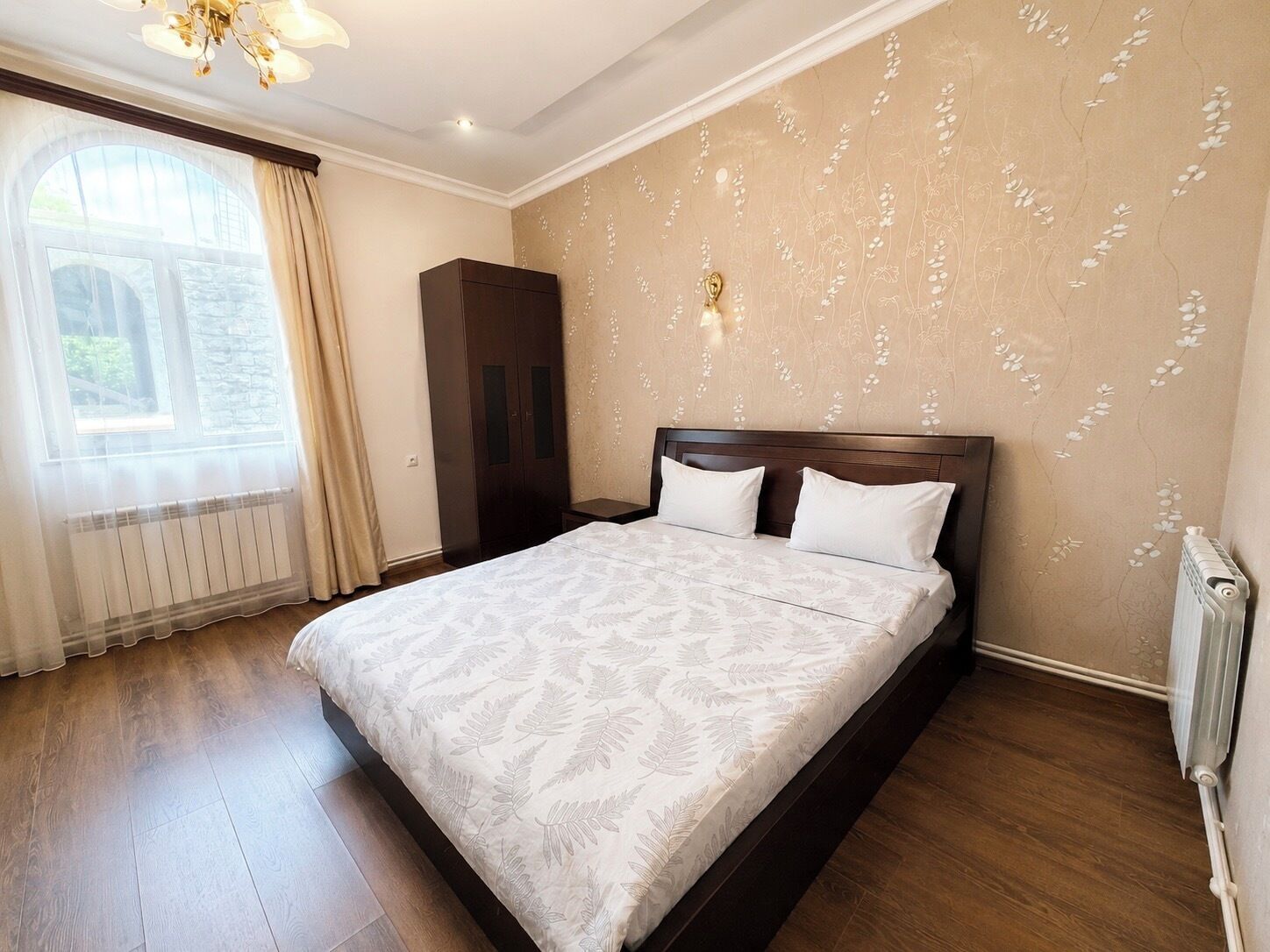 A hotel room with a large bed, a wardrobe, a radiator, and a window with curtains.