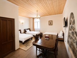 Una habitación con dos camas, una mesa de comedor, un candelabro, un muro de piedra y un televisor.
