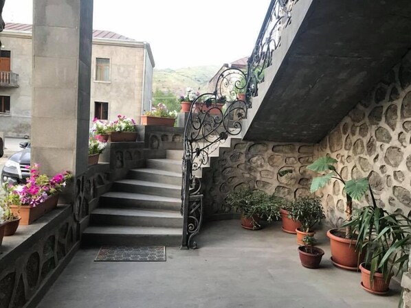 A stone staircase with a wrought iron railing leading to a balcony, surrounded by potted plants and flowers. - Christy Hotel (Goris)