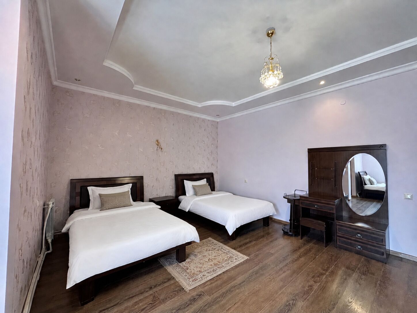 Une chambre d’hôtel avec deux lits simples, une commode en bois, un miroir et un lustre.