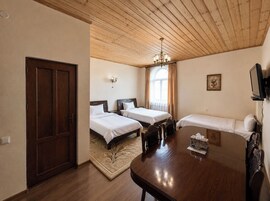 Habitación de hotel con techo de madera, dos camas individuales, un sofá, una mesa de comedor y un televisor.