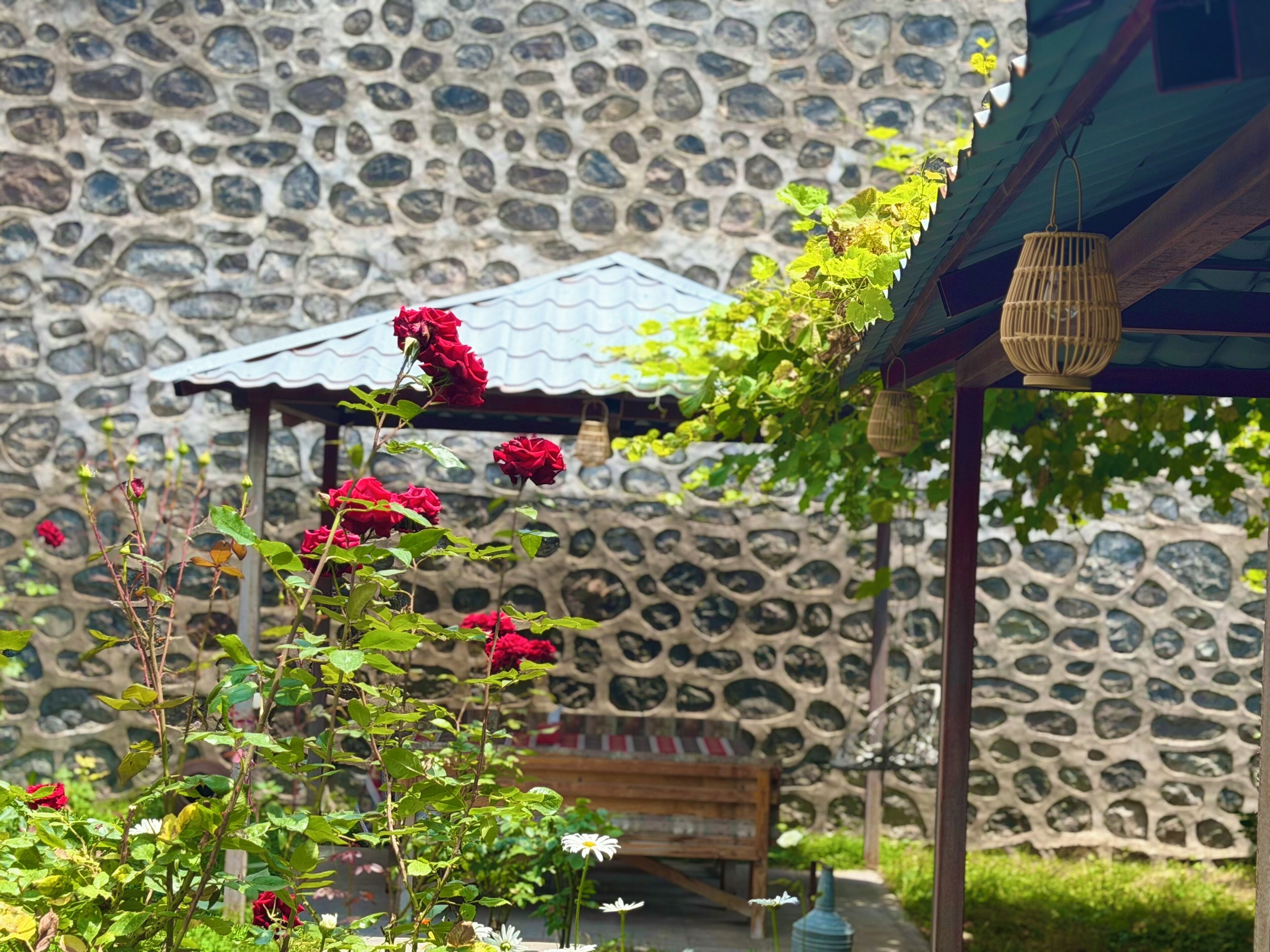 Un muro de piedra con una pérgola de madera y un banco.