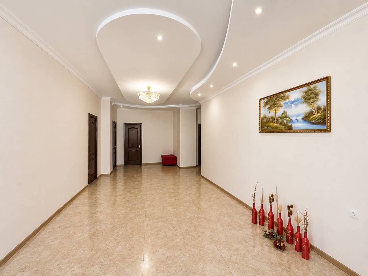 Um corredor amplo com piso lustroso, um candelabro e um quadro na parede.