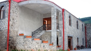 A stone building with a curved facade, a central staircase, and multiple flower planters. - Christy Hotel (Goris)