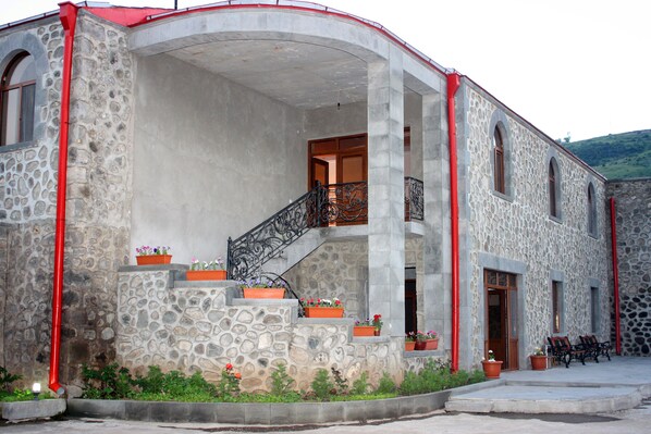 Un edificio de piedra con fachada curva, una escalera central y varios maceteros con flores.