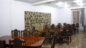 A dining area with a stone wall, wooden tables, and chairs. - Christy Hotel (Goris)