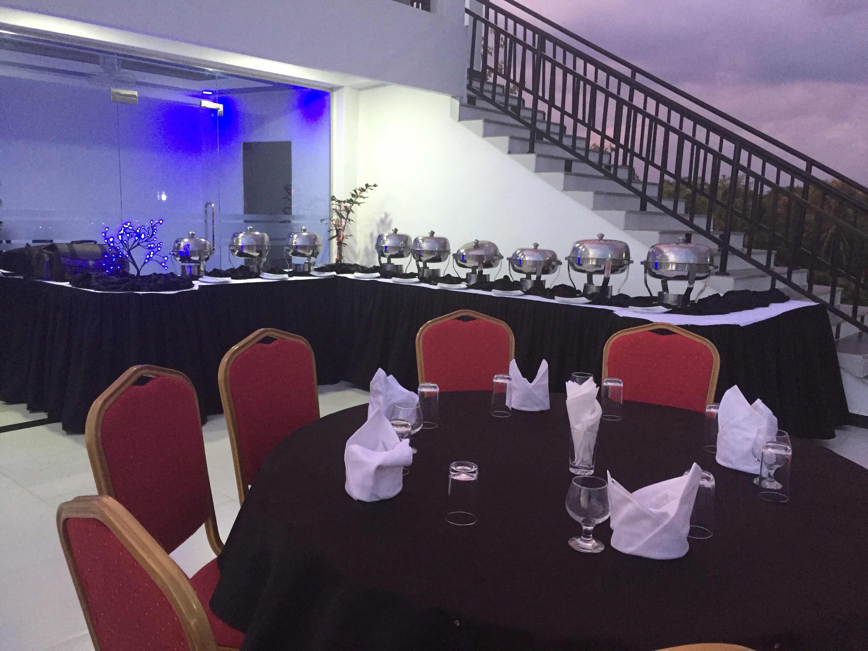 Un salón de conferencias con una larga mesa dispuesta para una reunión, una escalera al fondo y una pared iluminada en azul.