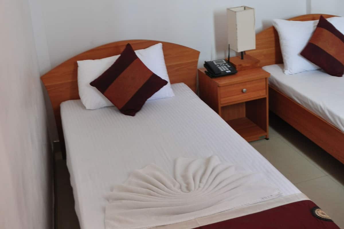 Ein Hotelzimmer mit zwei Einzelbetten, jeweils mit einem Holz-Kopfstück, einem Nachttisch mit Lampe und einem gerahmten Bild an der Wand.