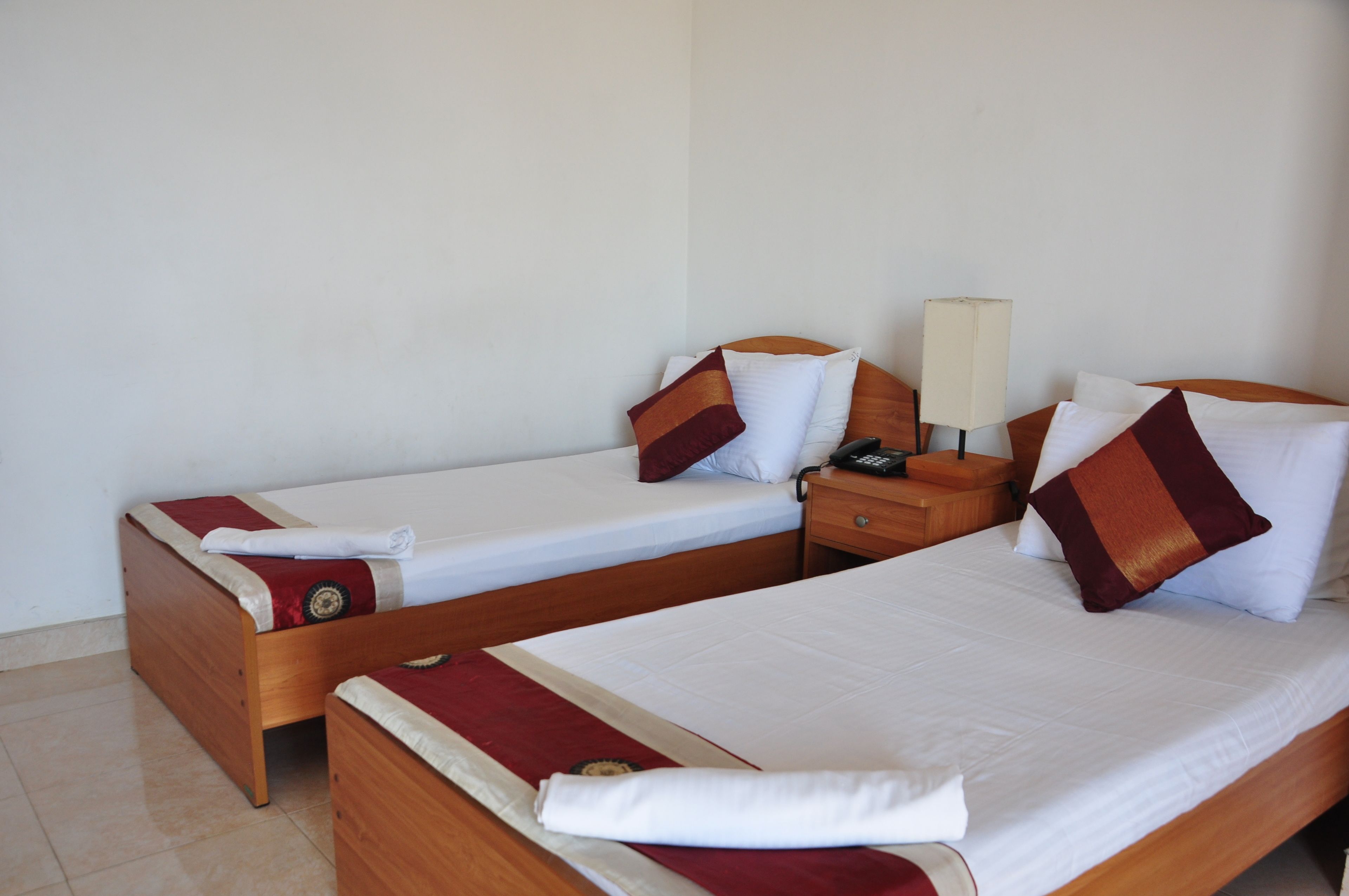 A hotel room with two single beds, wooden headboards, white linens, and a bedside table with a lamp.