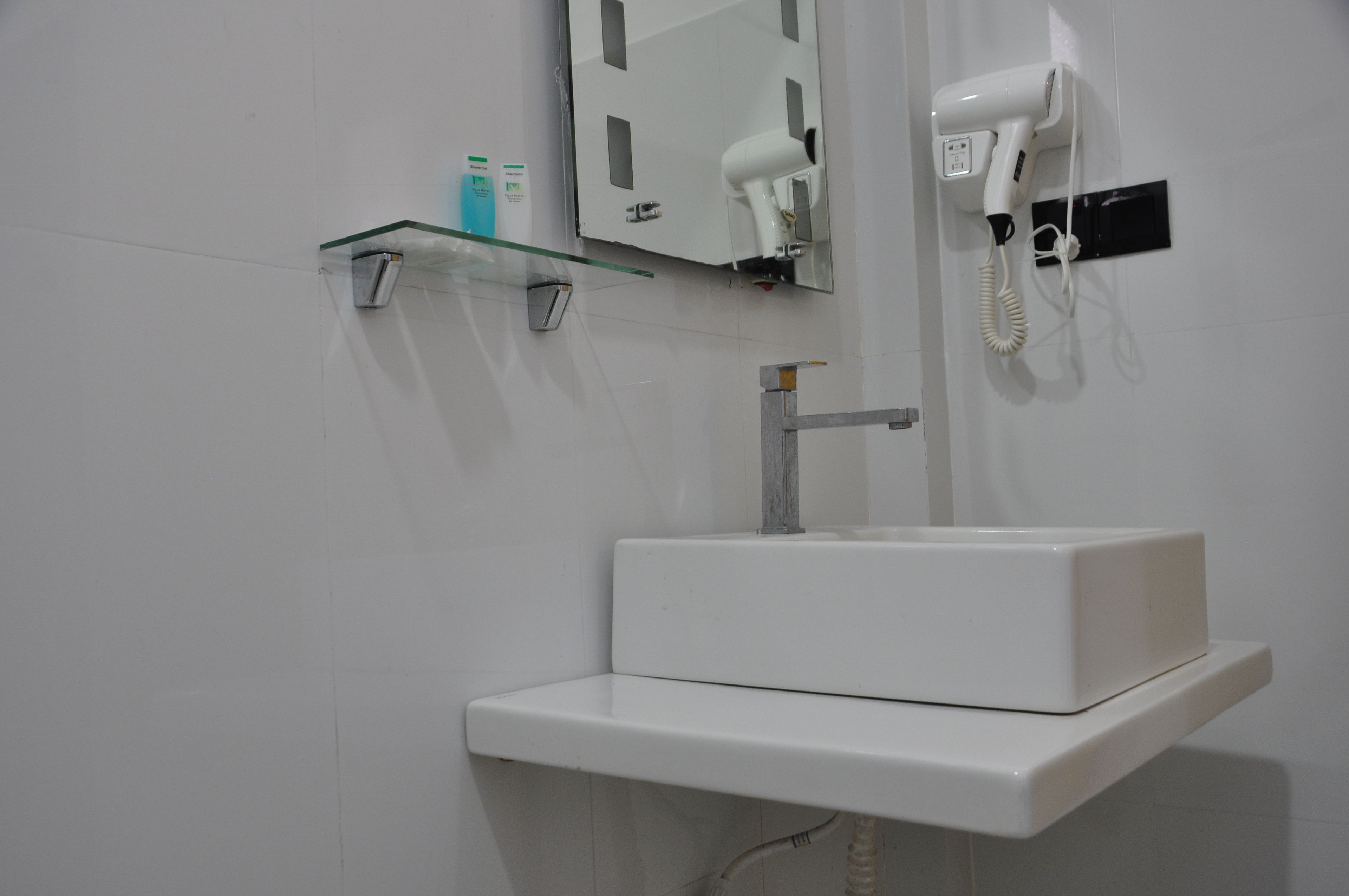 A bathroom with a white sink, a glass shelf with toiletries, a hairdryer, and a mirror.