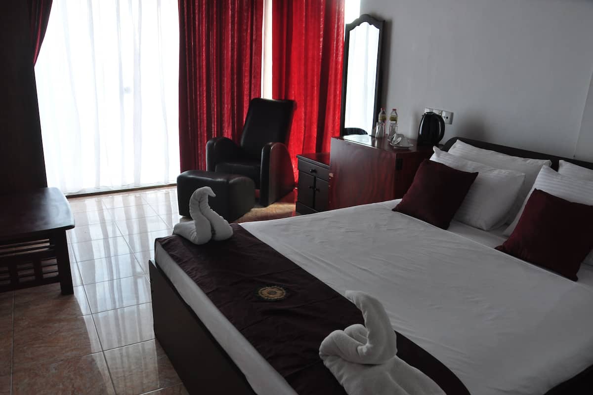Ein Hotelzimmer mit einem großen Bett, roten Vorhängen, einem Schreibtisch, einem Stuhl und einem Spiegel.