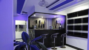 A modern kitchen with a black countertop, three bar stools, and a window with blinds. - Villa Hotel (Trincomalee)