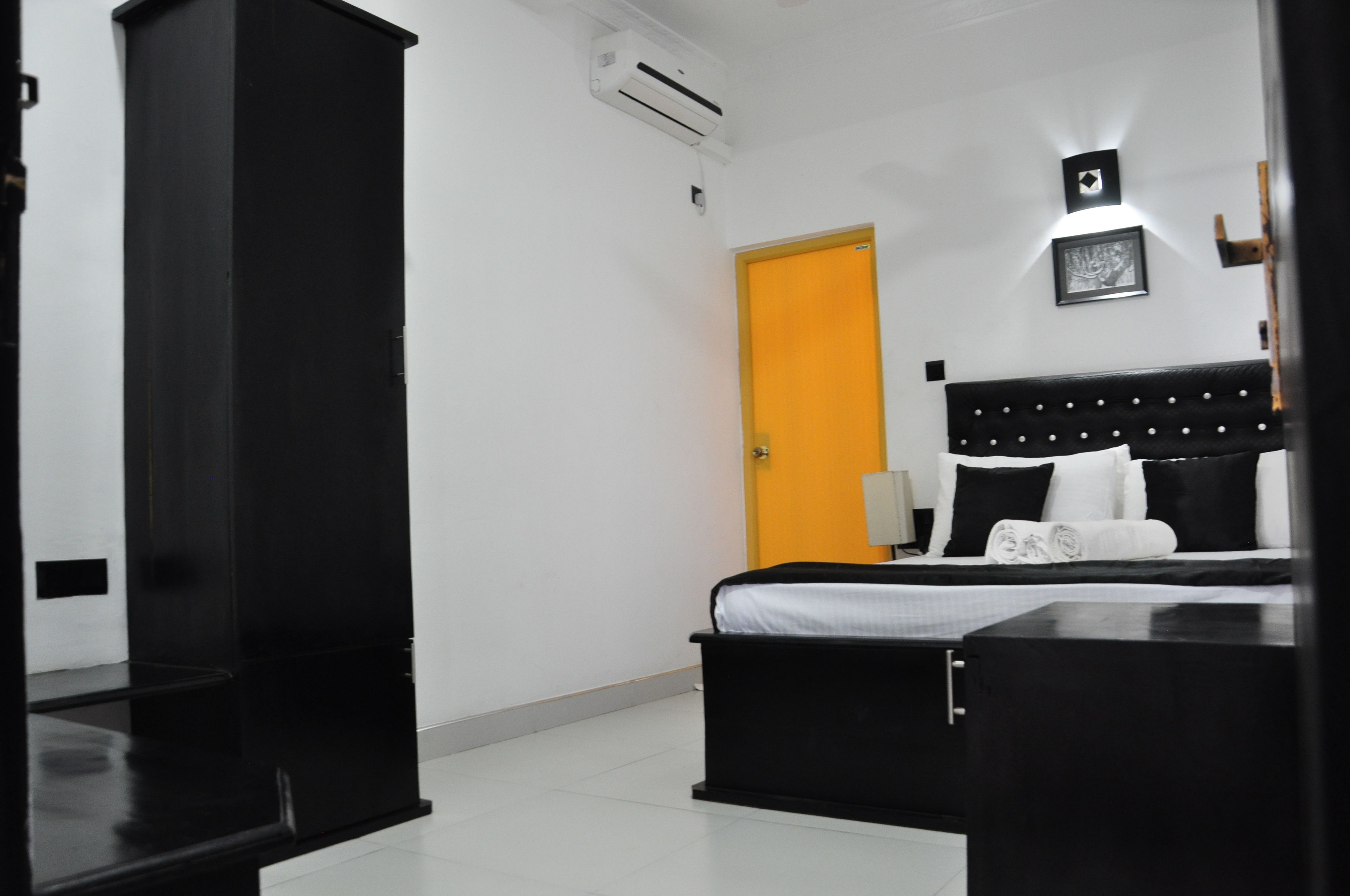 A hotel room with a bed, a wardrobe, a desk, and an air conditioning unit.