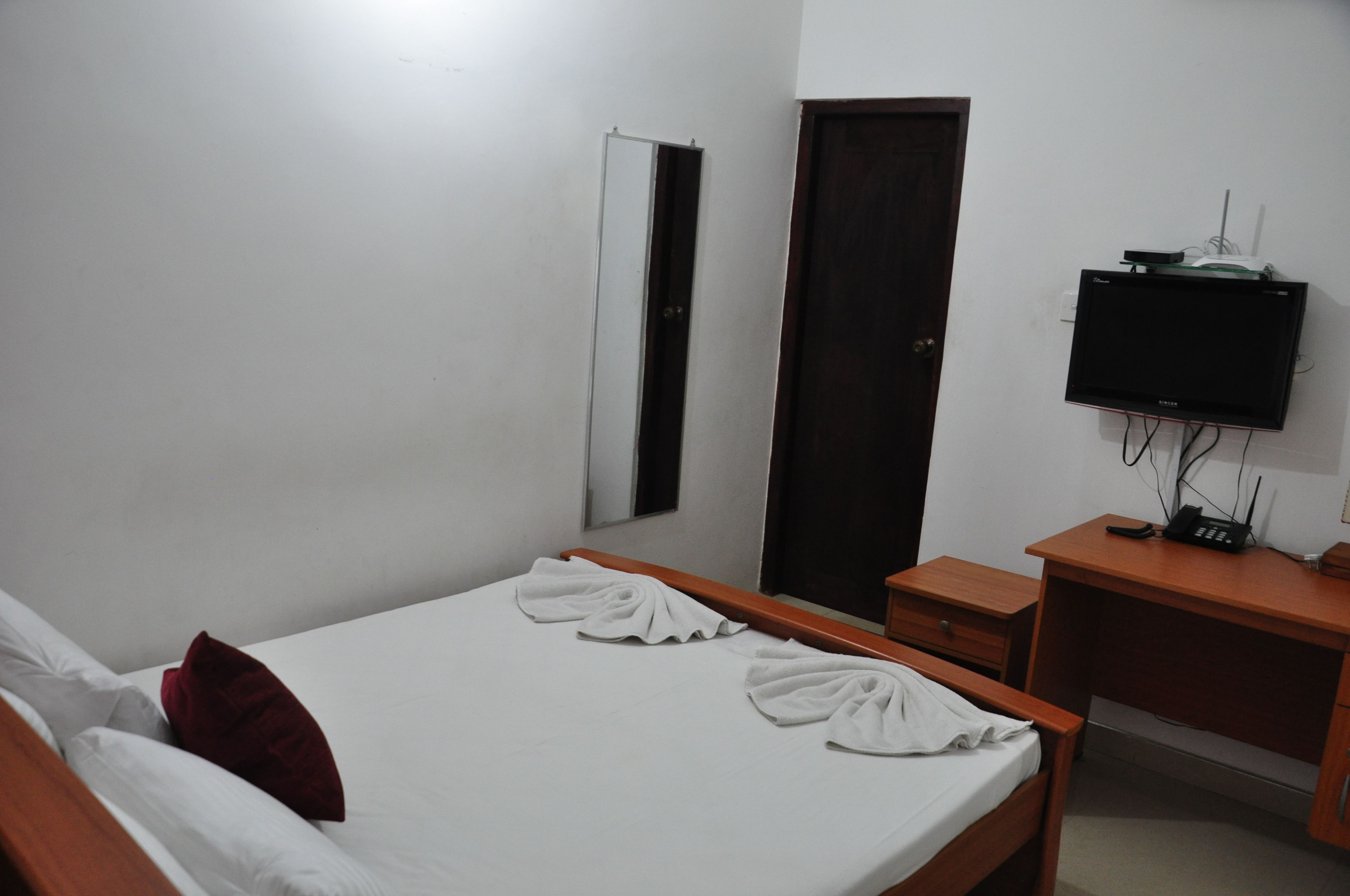 Een hotelkamer met een bed, een houten bureau, een televisie en een kledingkast.