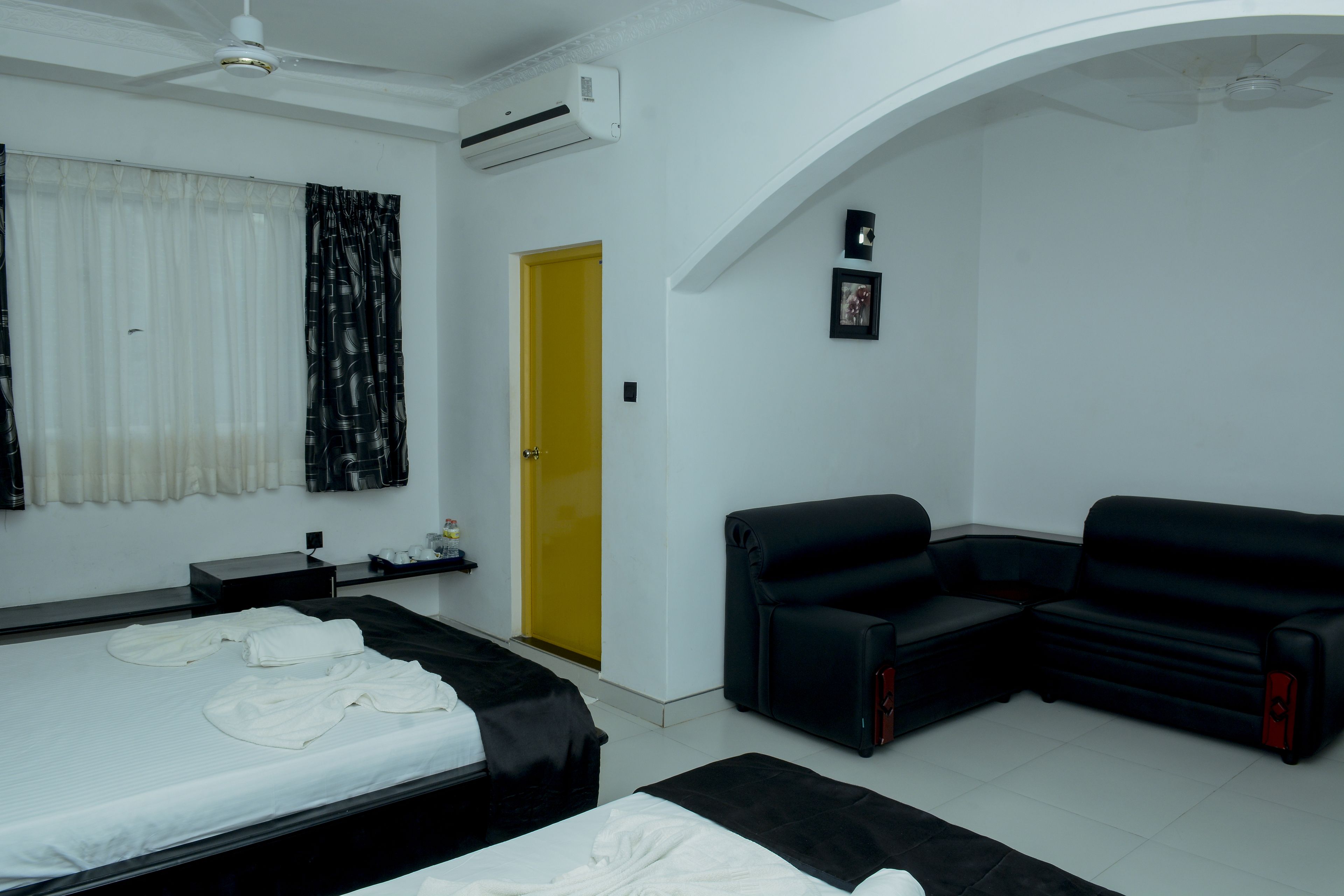 A hotel room with a bed, a black sofa, a yellow door, and an air conditioning unit.