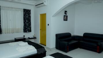 A hotel room with a bed, a black sofa, a yellow door, and an air conditioning unit.